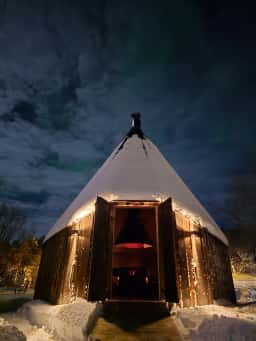 Lavvu with snow on the roof at night, fire lit inside